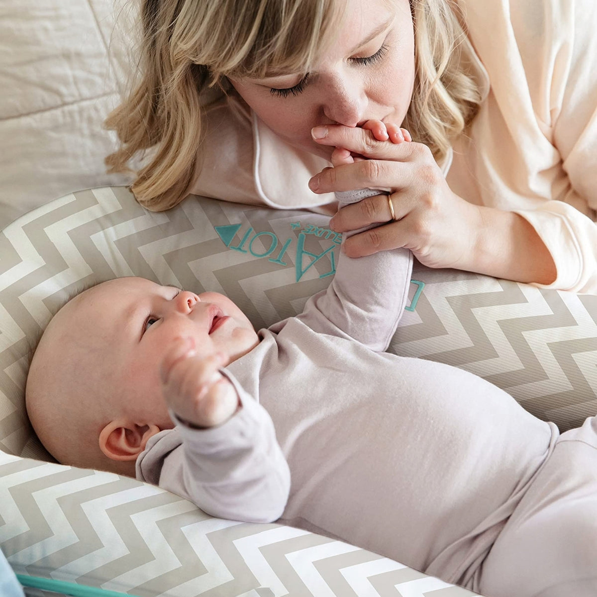baby laying in DockATot Deluxe+ Baby Dock in Silver Lining with mother holding its hand