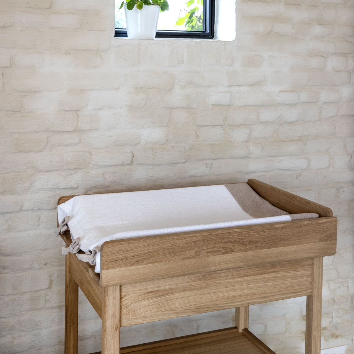 FSC certified solid oak wooden baby changing table with a comfy white changing pad set in a premium European nursery against a stone wall.