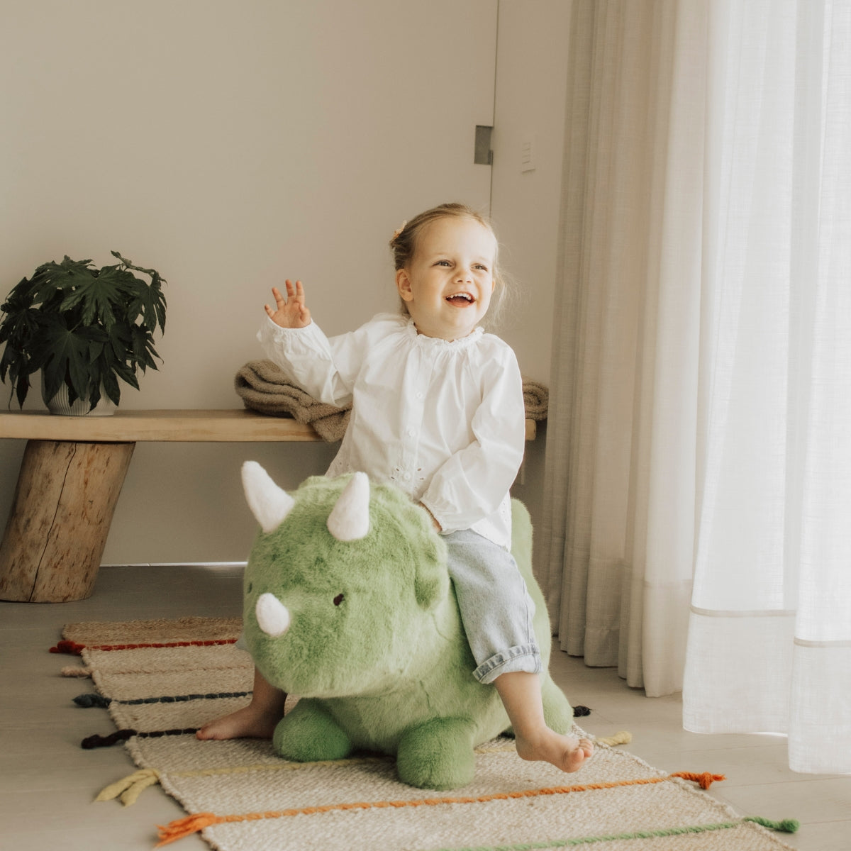 yound child riding a Wild & Soft Bouncy Dino soft plush ride-on dinosaur toy in modern home
