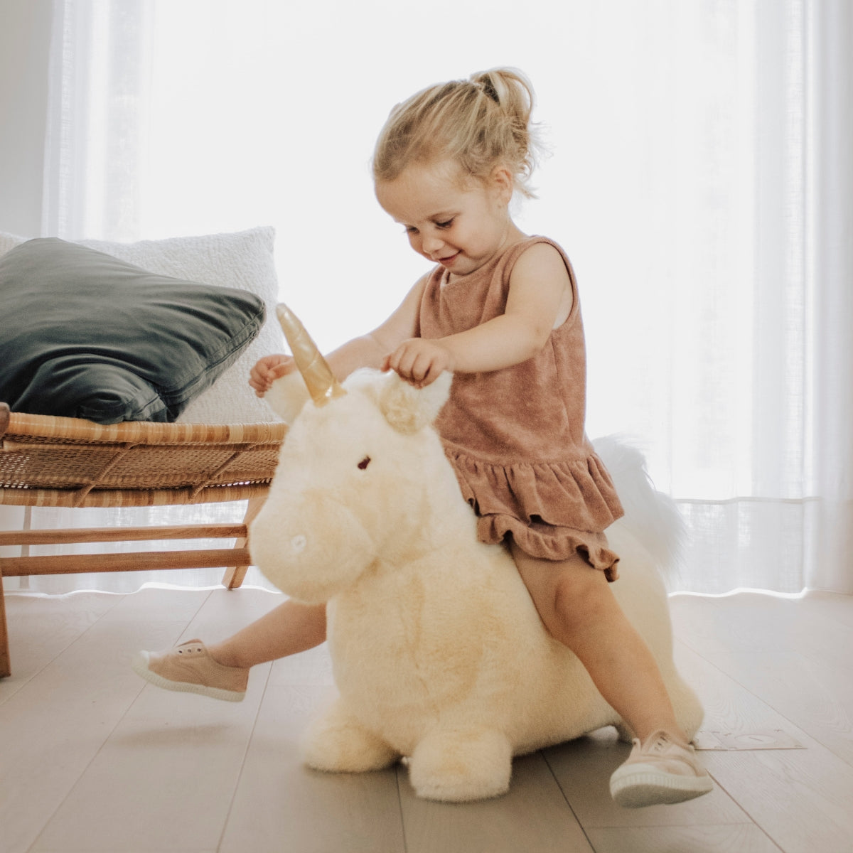 a young girl sat on a Wild & Soft beige unicorn ride on bouncer in a modern living space