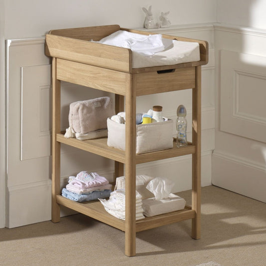 Natural oak baby changing table with drawer and open storage shelves in a nursery