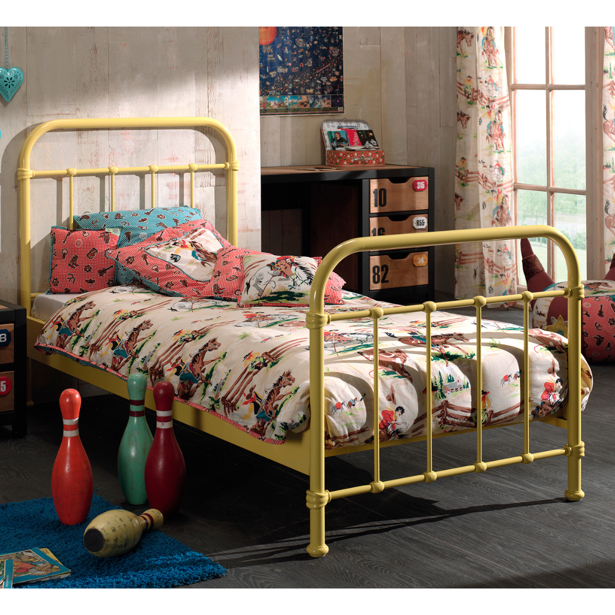 Kids sturdy looking yellow metal bed frame with colorful bedding in a room with a desk and window.