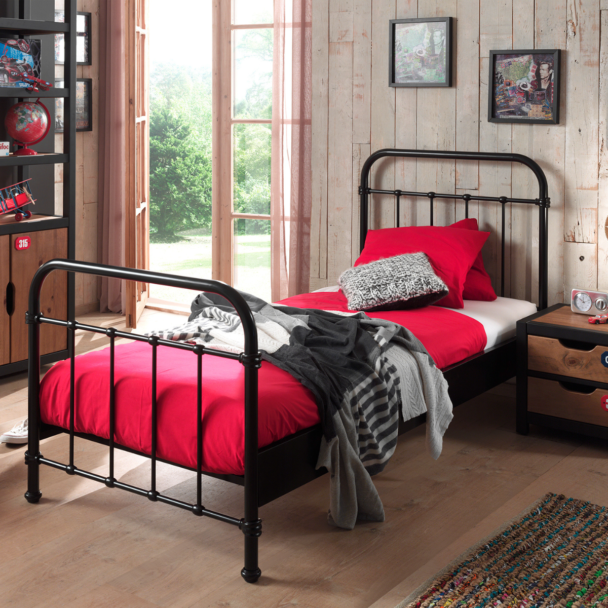 Bedroom with a black metal frame single bed and red bedding, wooden floor, and window.