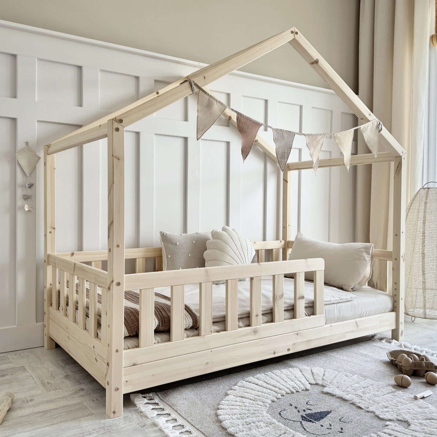 Children's wooden house-shaped bed with bedding and pillows in a room setting.