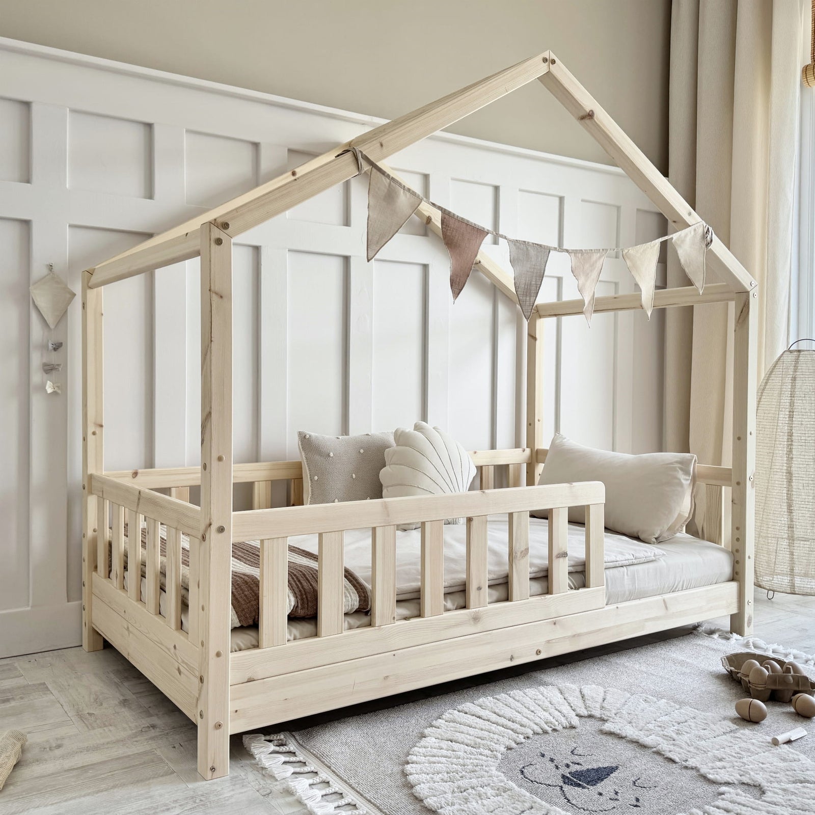 Children's wooden house-shaped bed with bedding and pillows in a room setting.