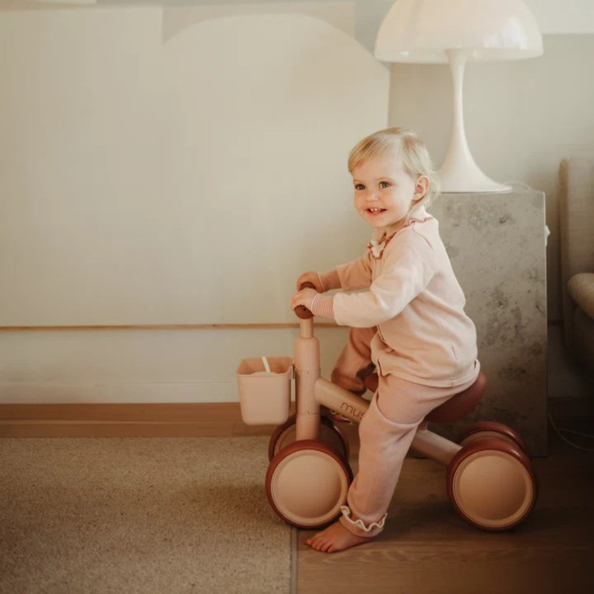 small childing riding a Mushie Mini Toddler Bike in Blush with EVA wheels in modern home