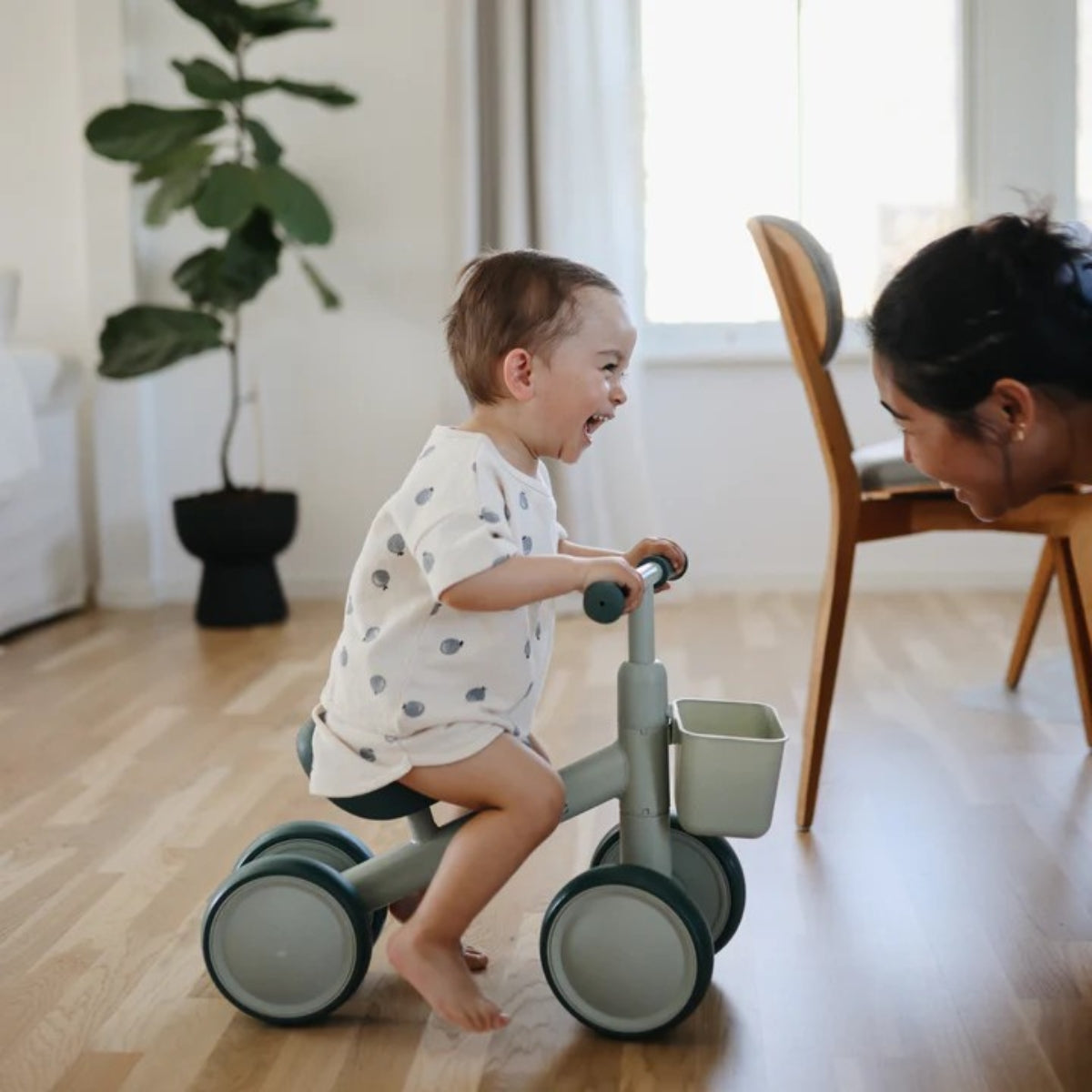 toddler riding Mushie Mini Toddler Bike in Sage in modern living space