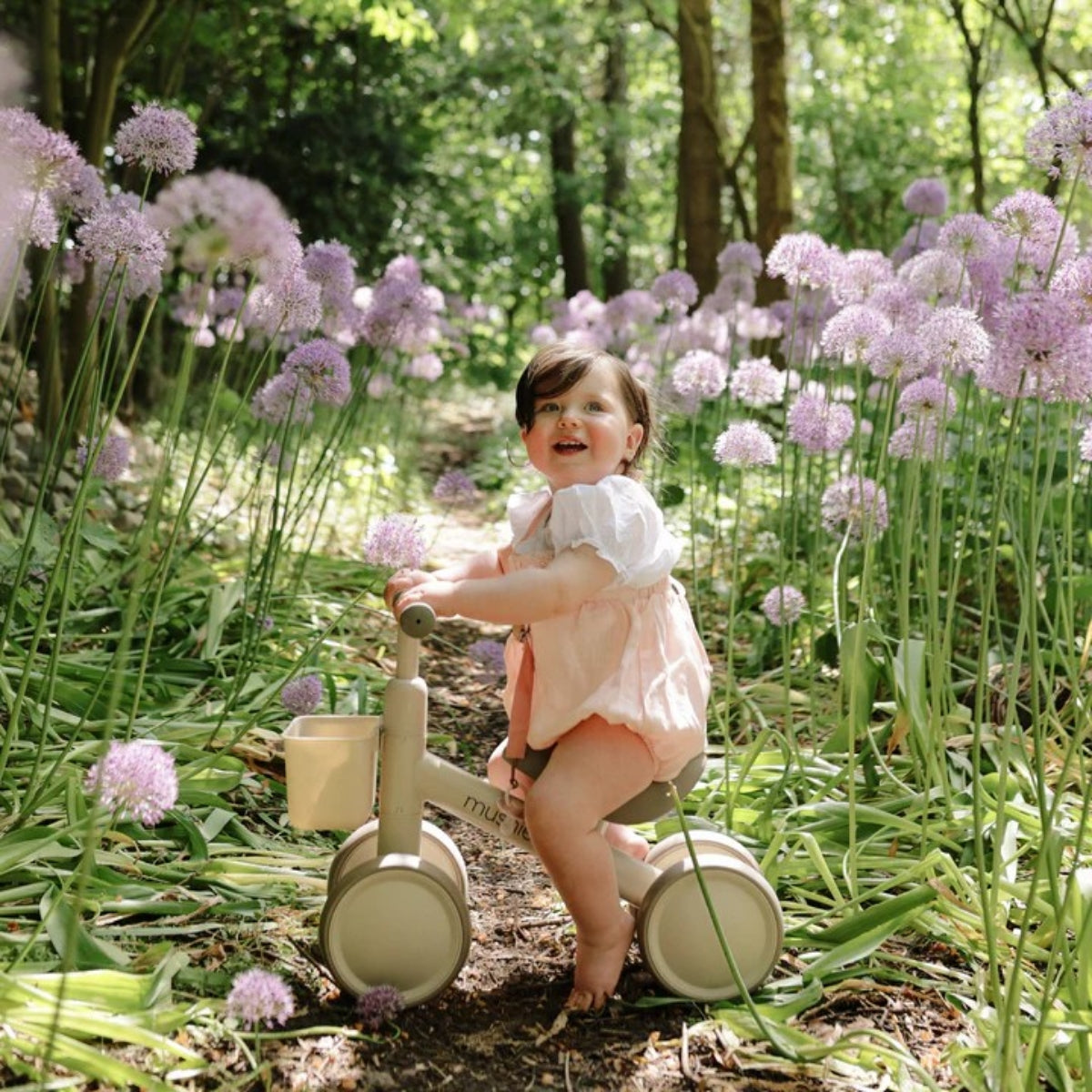 child riding Mushie Mini Toddler Bike in Shifting Sand in garden