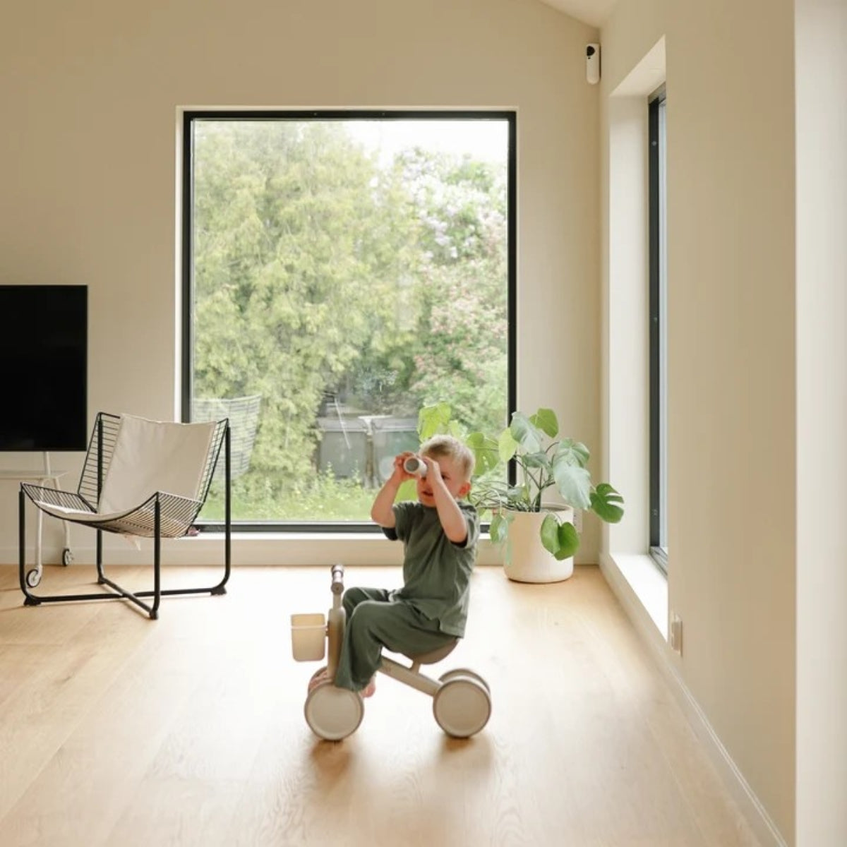 child riding Mushie Mini Toddler Bike in Shifting Sand in modern home