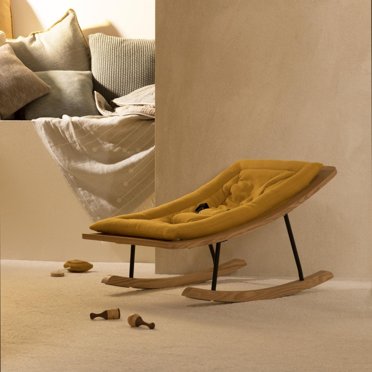 Quax Wooden Rocking Baby Bouncer in Saffron orange with natural ash wood rockers and padded seat in a neutral nursery setting