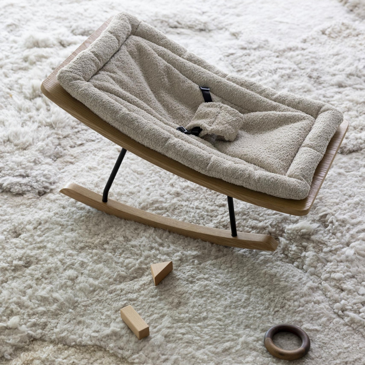Quax Wooden Rocking Baby Bouncer in sheep bouclé with natural ash wooden rockers and 3-point harness on a soft textured rug