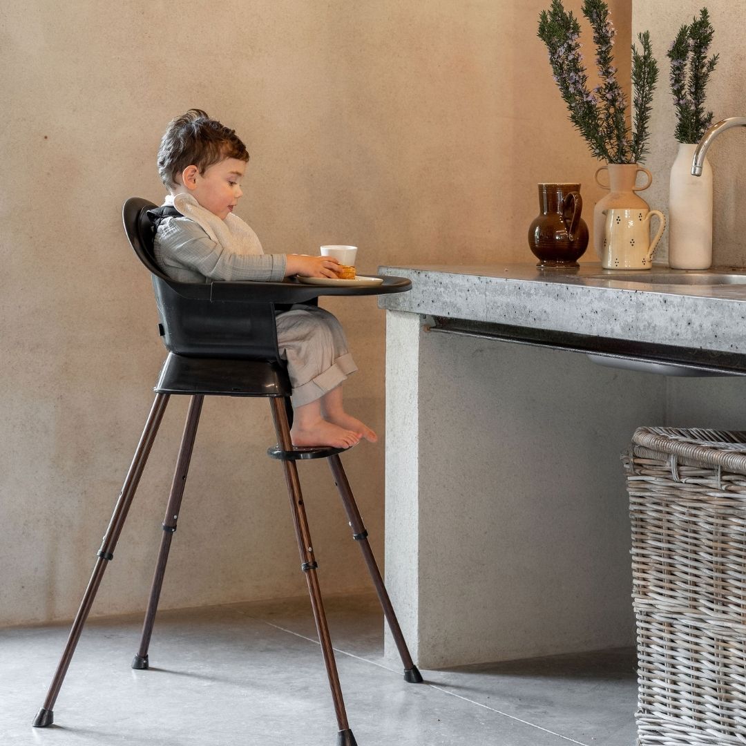 Child sitting in a quax black high chair at a kitchen counter with a neutral background