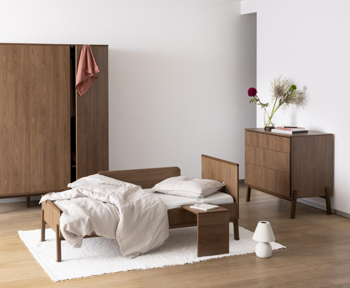 Quax Ashi Chestnut cot bed converted into 170x70cm junior bed with matching wardrobe and drawers in child's bedroom with neutral decor
