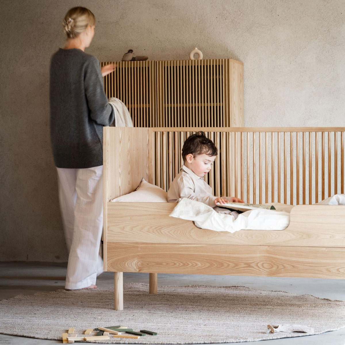 young sitting in a Quax Hai No Ki 140 x 70cm cot bed converted to toddler bed with safety rail in japandi inspired nursery