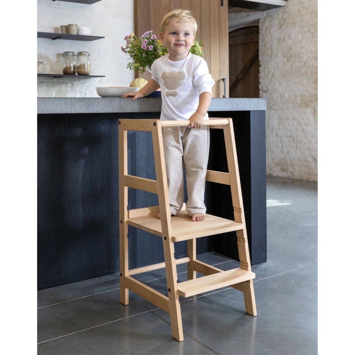 happy child standing on a Vipack Jaxx Toddler Learning Tower made from natural wood in modern European kitchen