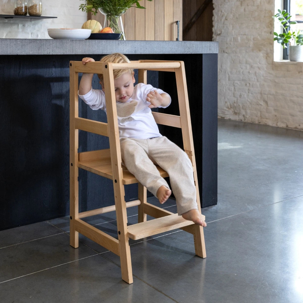 child getting on to sturdy looking vipack jaxx toddler learning tower in modern European kitchen