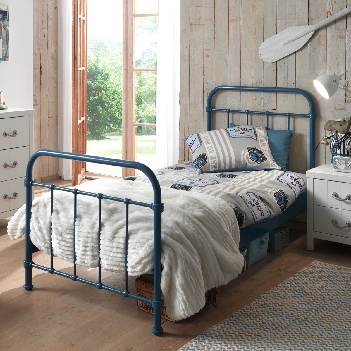 kids Blue metal single bed with white bedding in a room with wooden walls and large windows. Strong solid sturdy looking blue single bed frame 