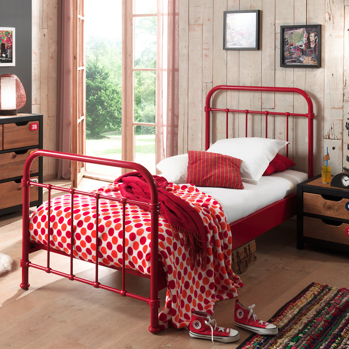 Kids Red metal single bed with white bedding and red polka dot blanket in a room with wooden floor and window.