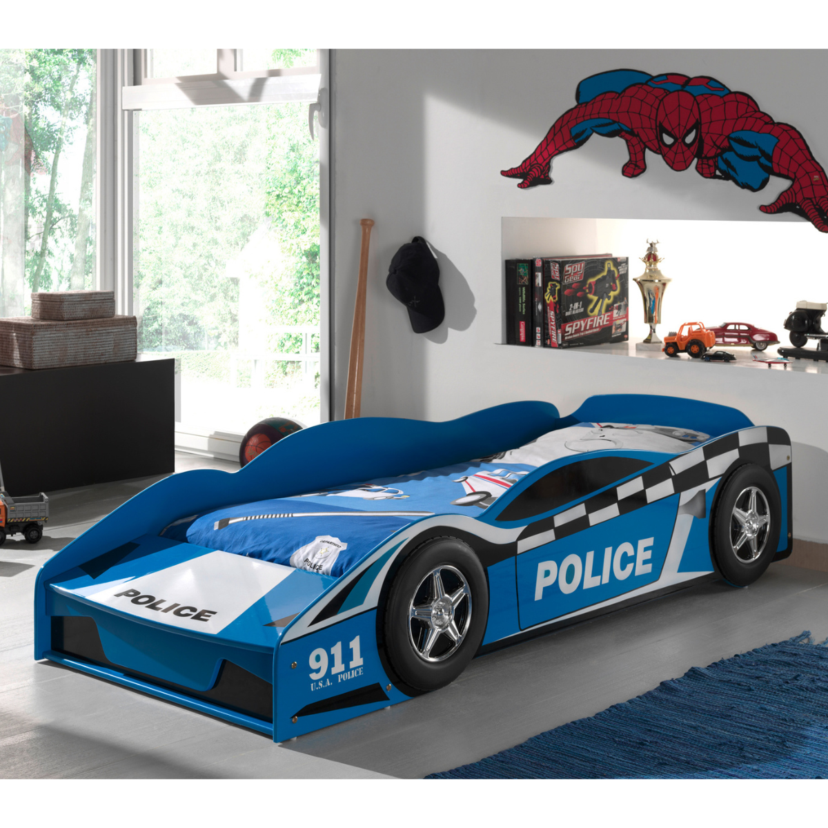 Children's police car 140x70cm toddler bed in a room with Spider-Man poster and toys. Lifestyle image of toddlers room with blue police car toddler bed