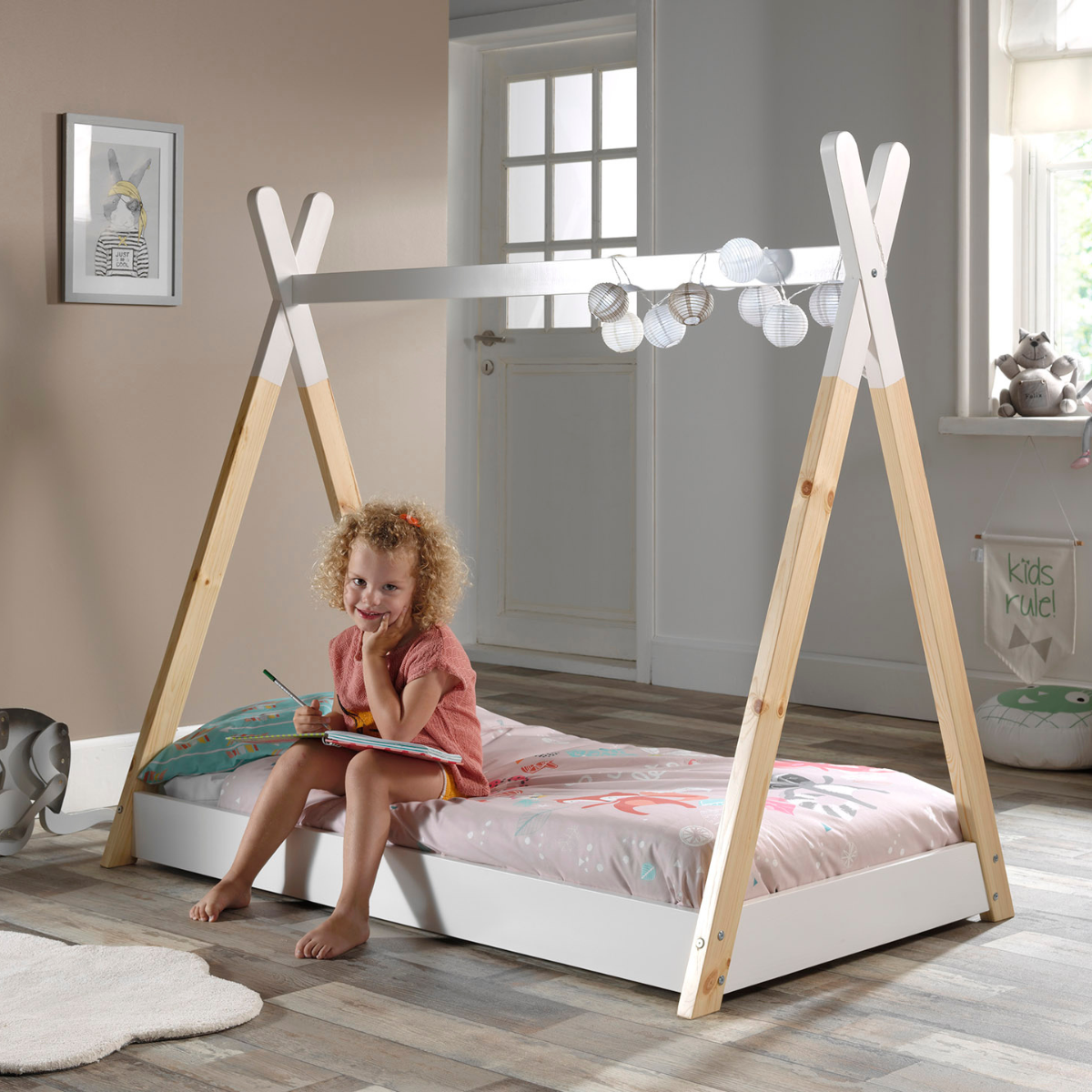 Child sitting on a VIPACK Sheila teepee-style floor bed in a bright room with natural light.
