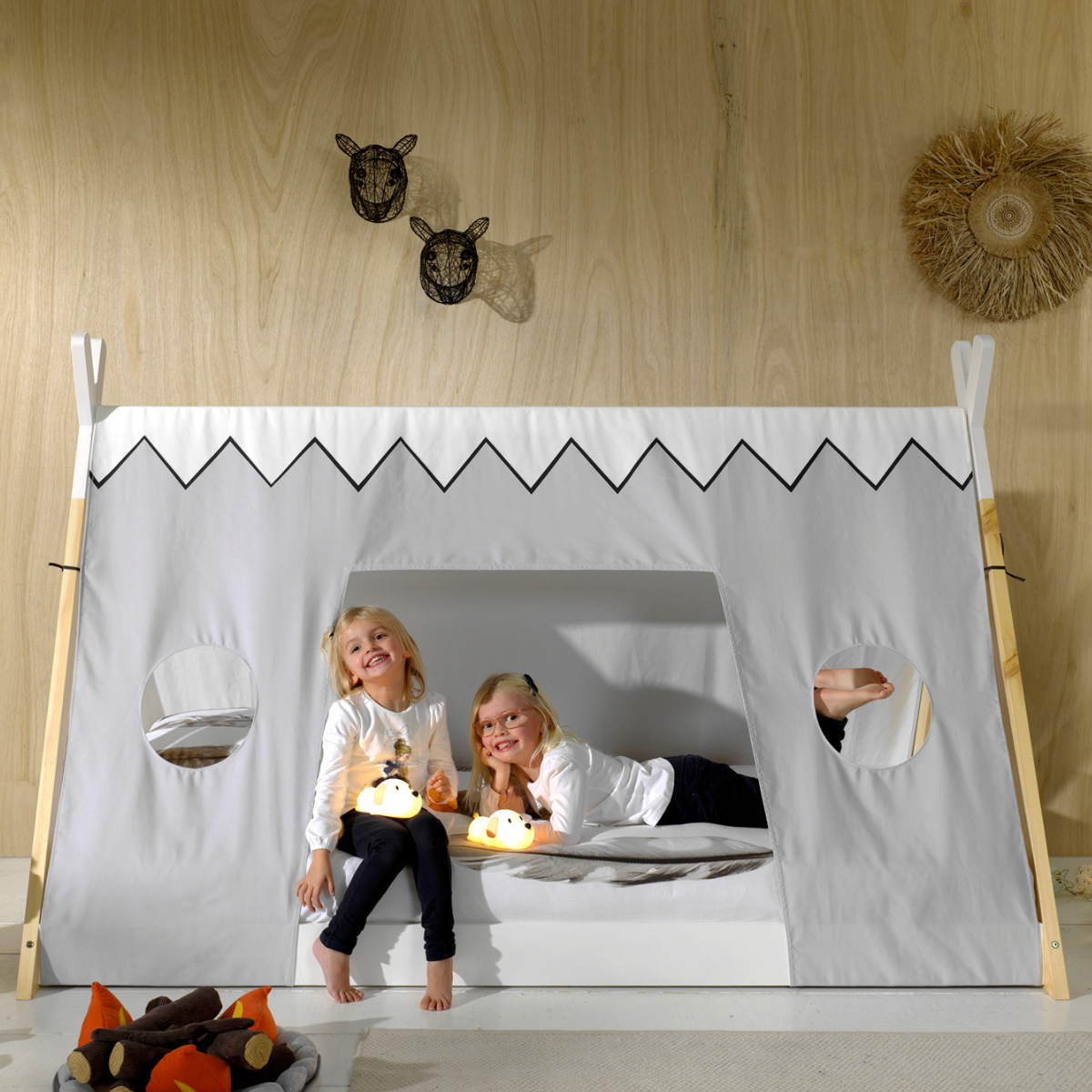 Two children playing inside VIPACK teepee bed with wooden frame against a wooden wall.