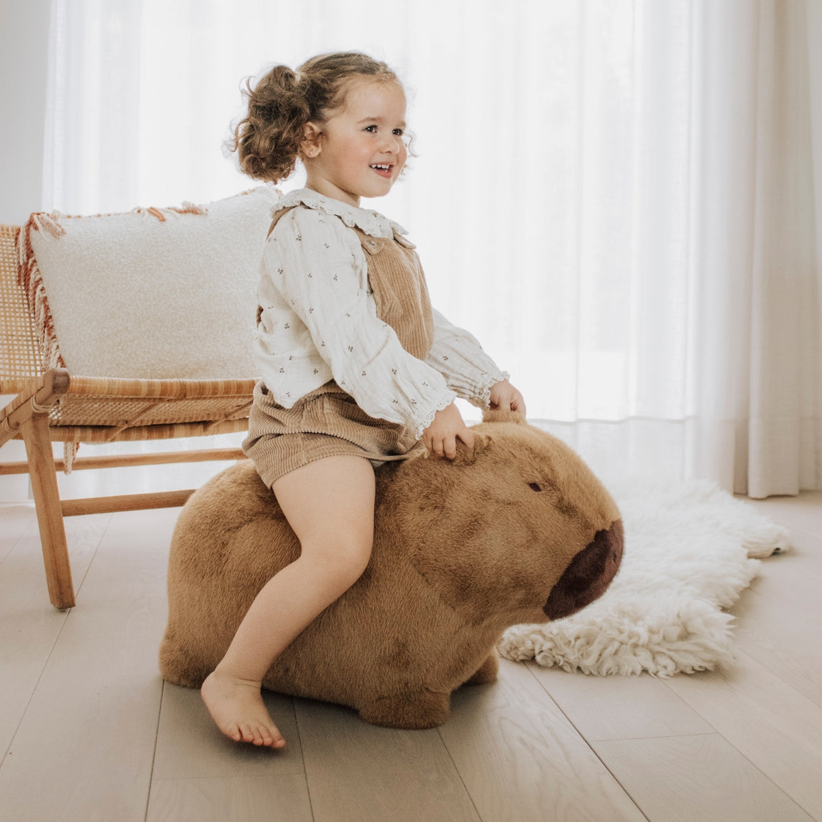 a young child sitting on a Wild & Soft Soft Bouncy Capybara plush bouncing toy for children in modern home