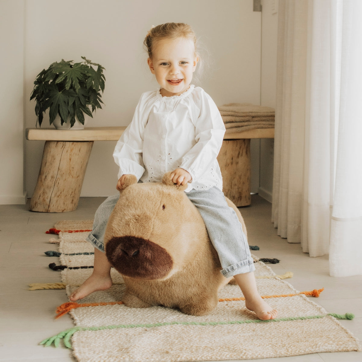 child riding Wild & Soft Soft Bouncy Capybara plush bouncing toy in living space