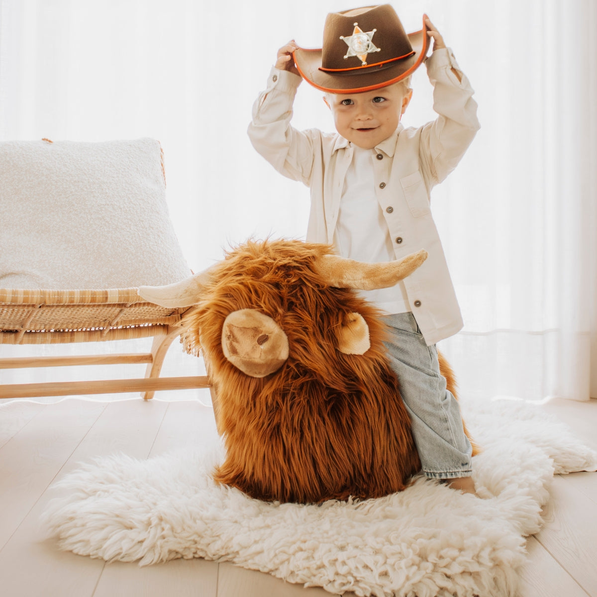 child sitting on a Wild & Soft Bouncy Highland Cow soft plush ride-on animal toy in cosy living room