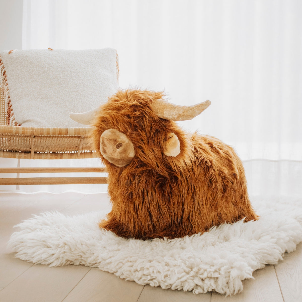 Wild & Soft plush Highland cow bouncing toy for children on plush cream rug in living room