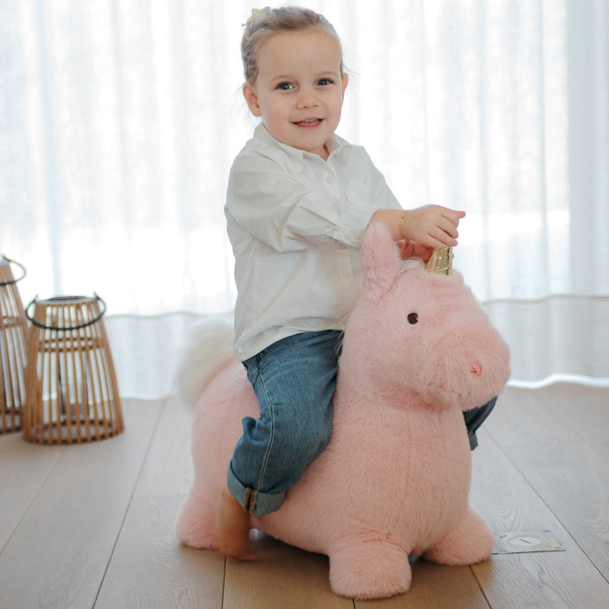 a young girl sitting on a Wild & Soft Soft Bouncy Pink Unicorn plush bouncing toy in modern home
