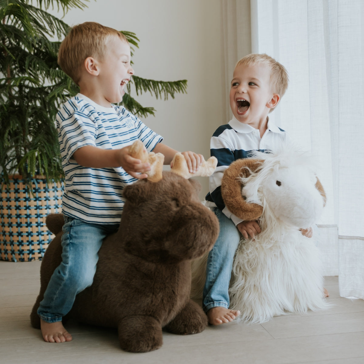 two young children playing on wild and soft plush animal bouncers in modern home