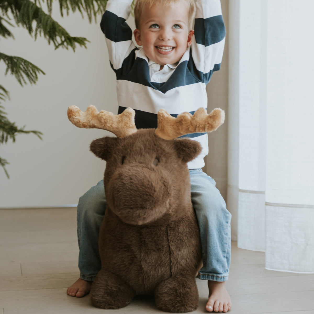 young child riding a Wild & Soft Soft Bouncy plush Moose ride on with antlers in modern living space