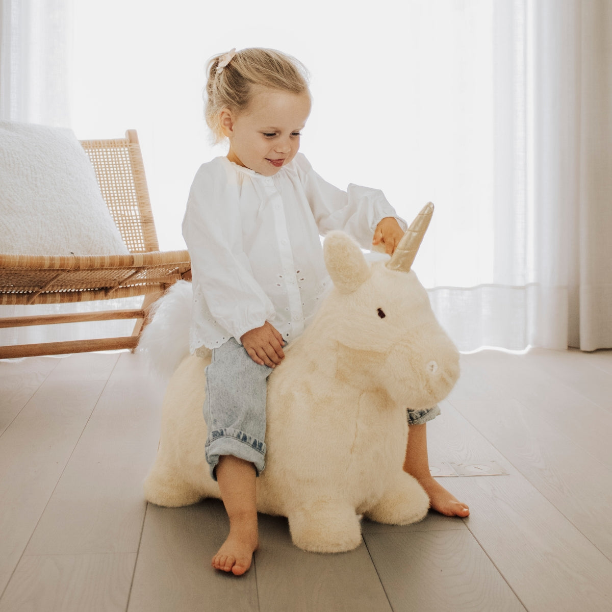 young girl sat on a Wild & Soft beige unicorn bouncer in her bedroom or playroom