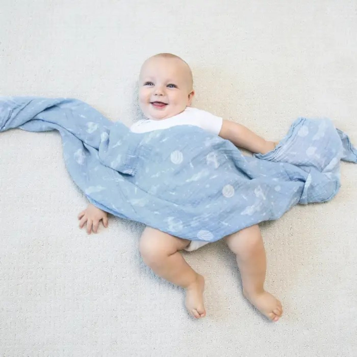 baby wrapped in blue aden + anais Essentials Cotton Muslin Swaddle Space Explorers design