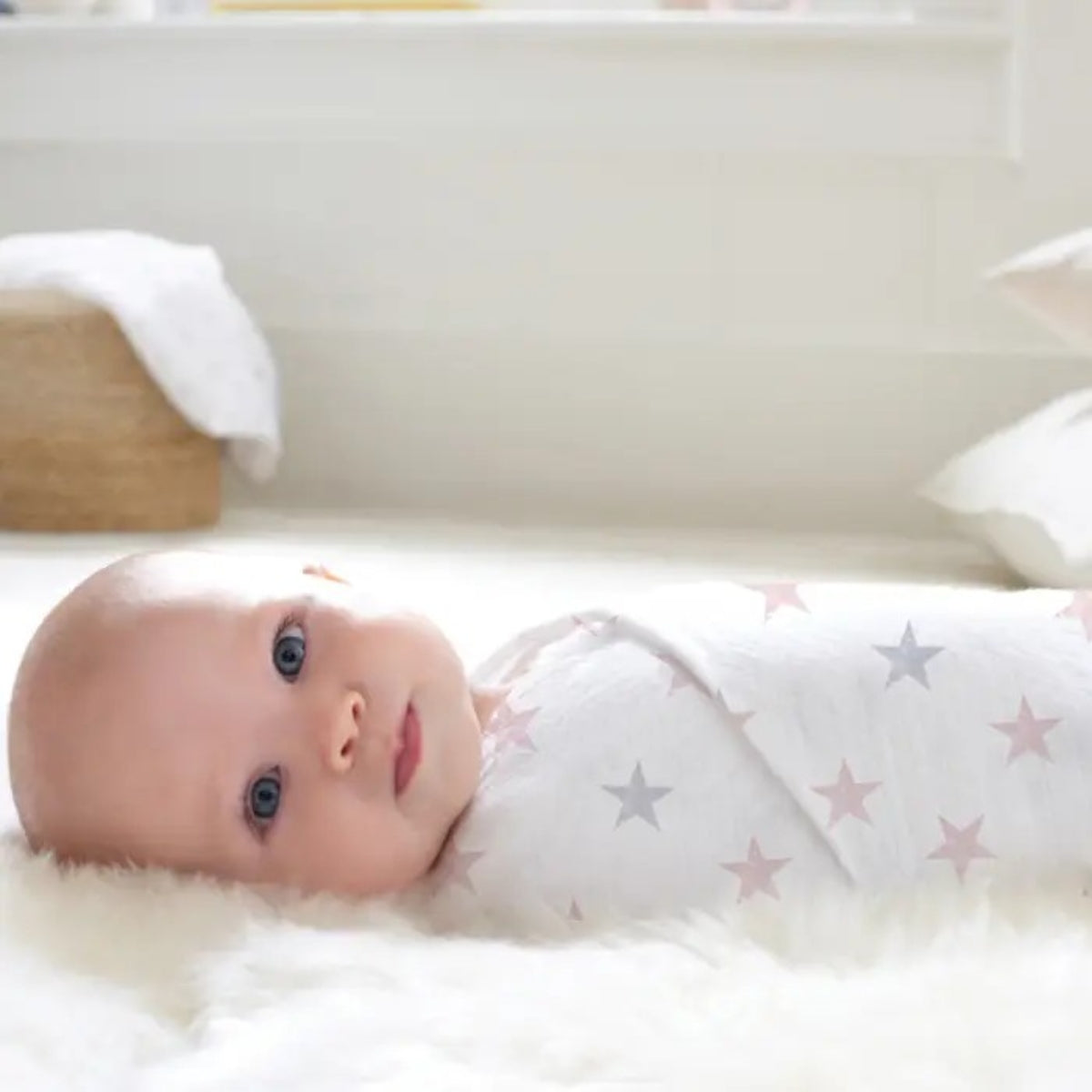Baby swaddled in a aden + anais cotton muslin blanket with star pattern on a soft surface