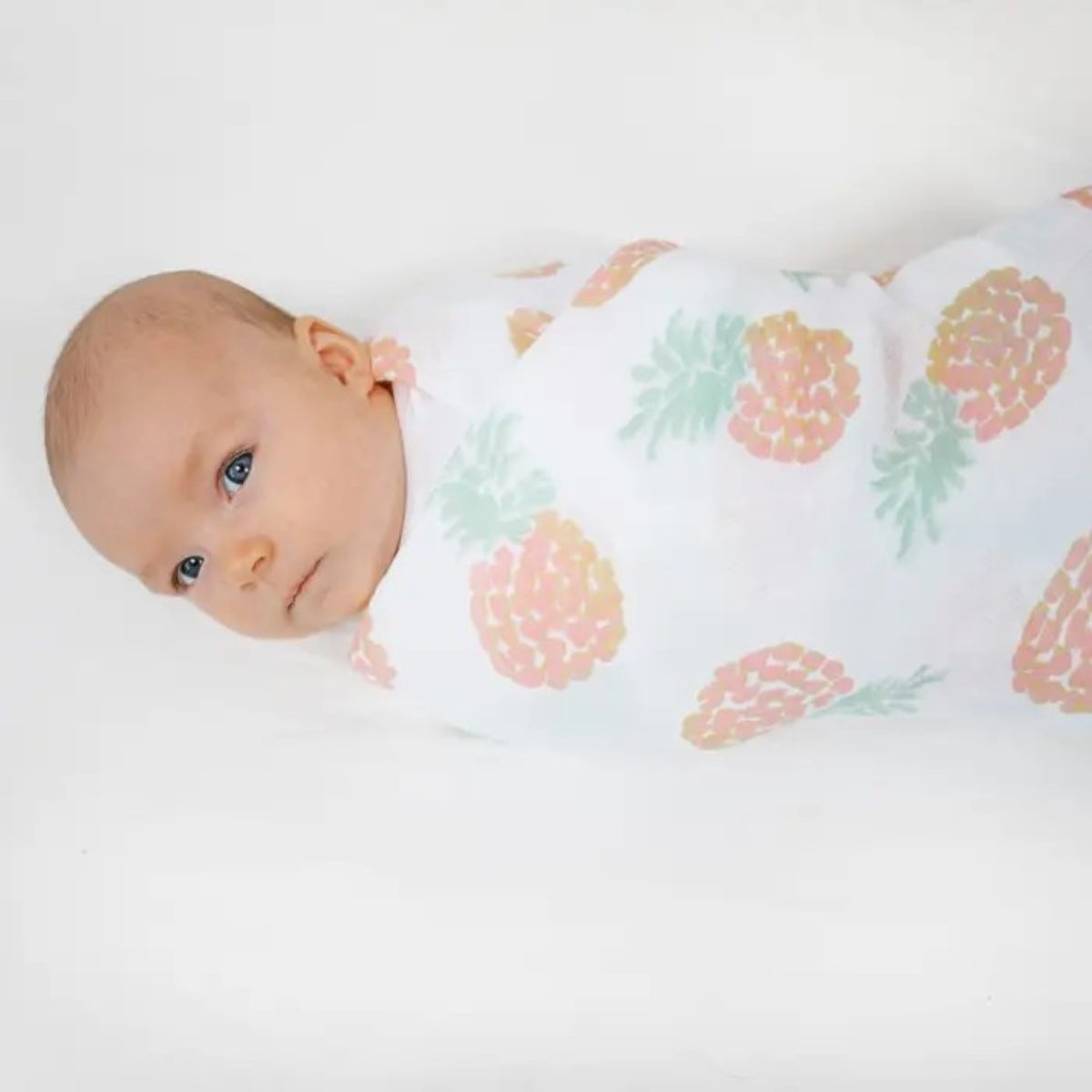 baby wrapped in aden + anais Tropicalia Essentials Cotton Muslin Swaddle Blanket with pineapples on