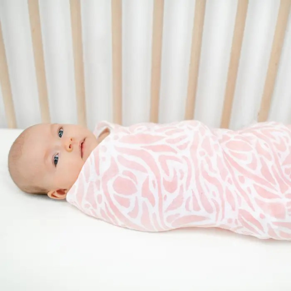 baby wrapped in aden + anais Tropicalia Essentials Cotton Muslin Swaddle Blanket with pink and white pattern