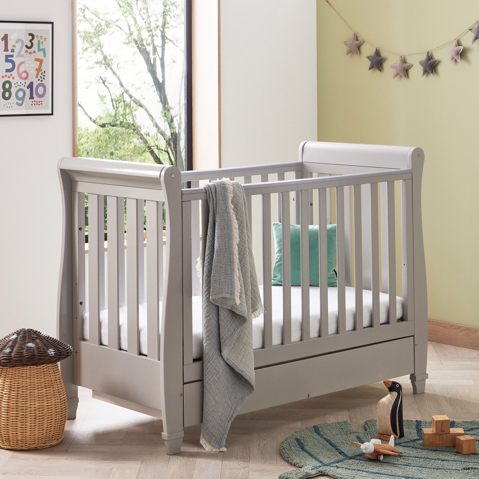 Babymore grey sleigh-style drop side cot bed with a drawer in a nursery with modern decor