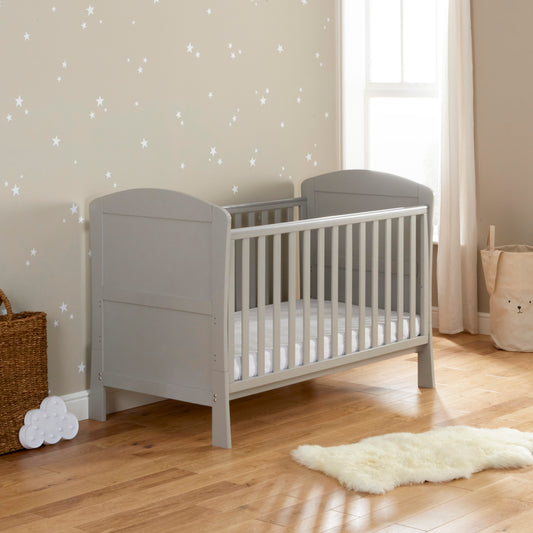 A grey Babymore Aston Drop Side Cot Bed 140xcm with a classic slatted design, situated in a nursery room with a white wall decorated with star stickers