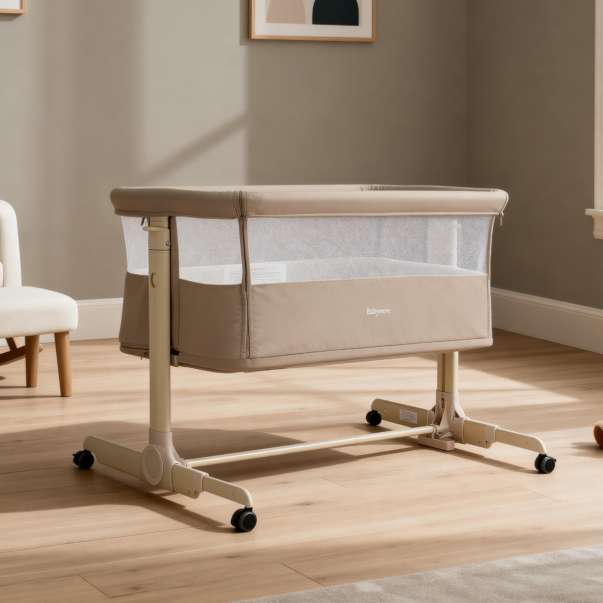 khaki babymore neera bedside crib on wheels in a room with wooden flooring and a neutral wall.
