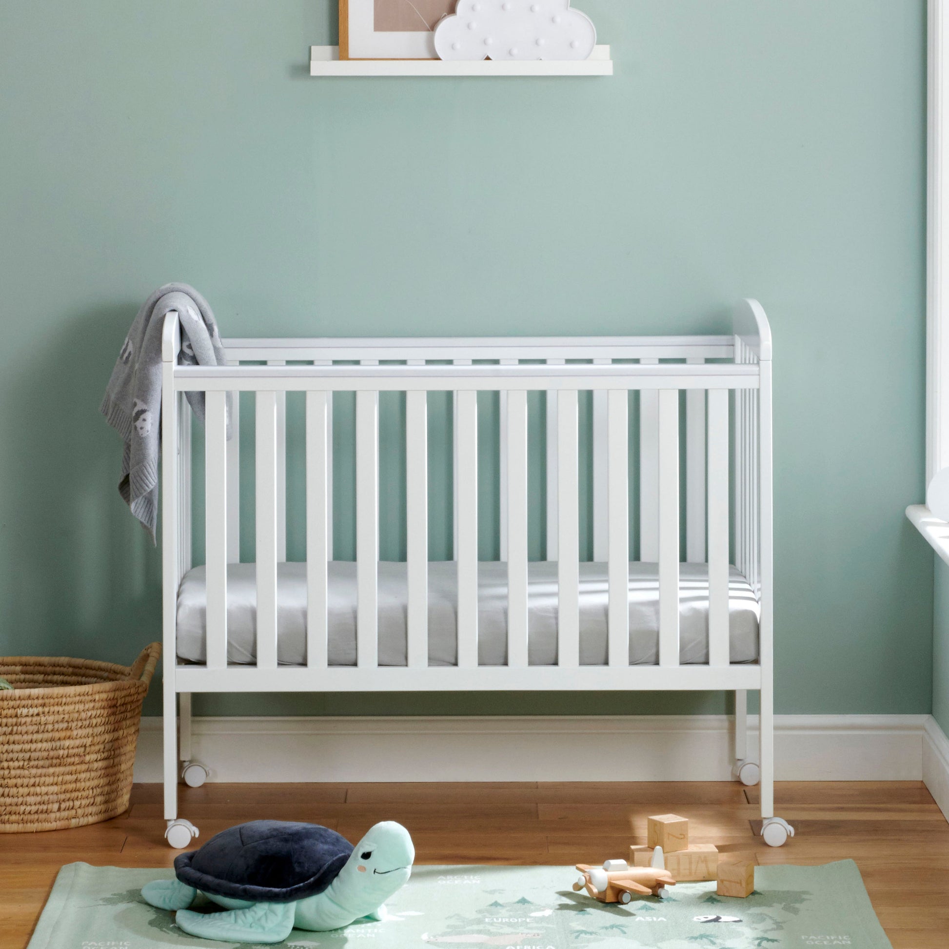 Babymore Space Saver Cot in white with lockable wheels and adjustable base in small room