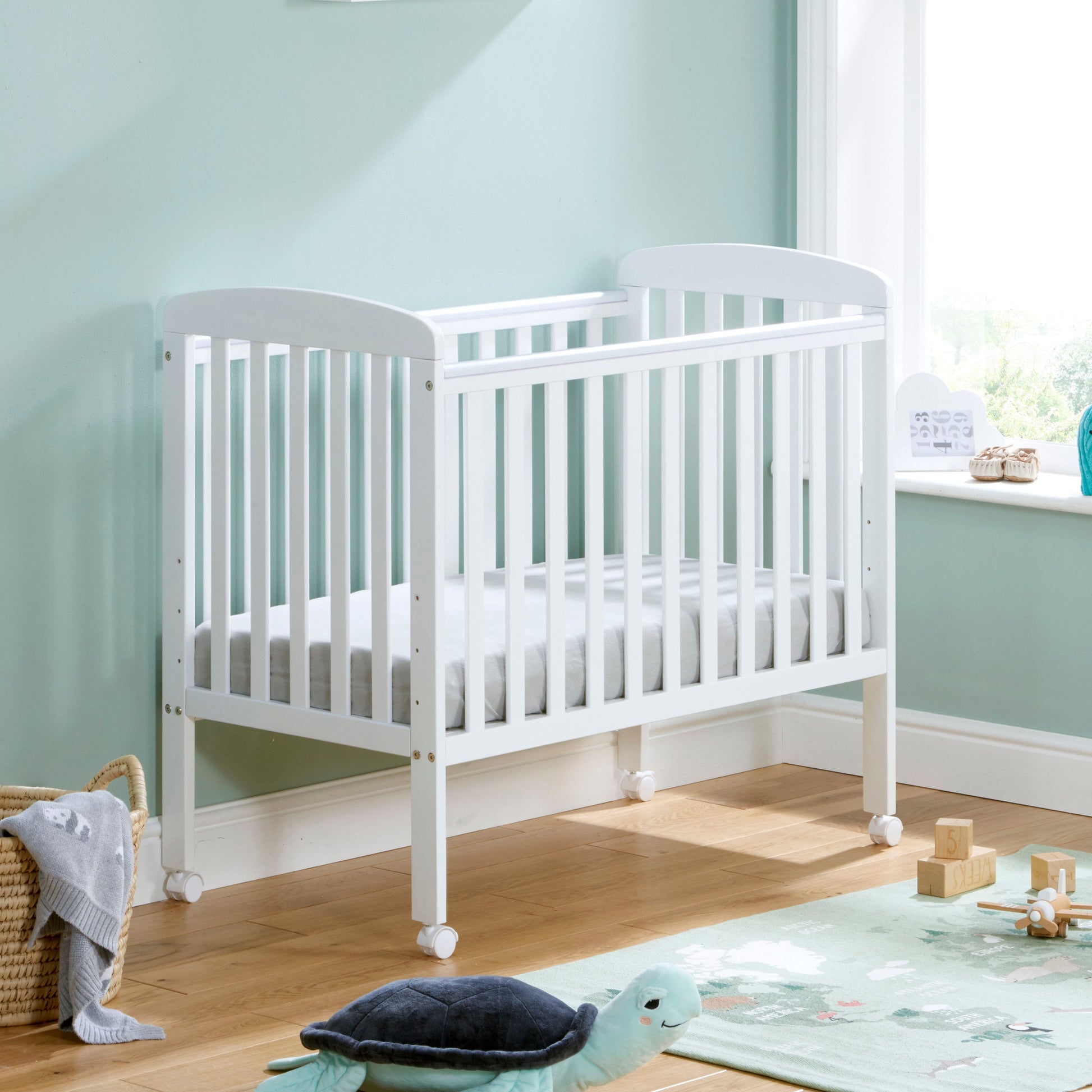 Babymore Space Saver Cot in white with lockable wheels and adjustable base.