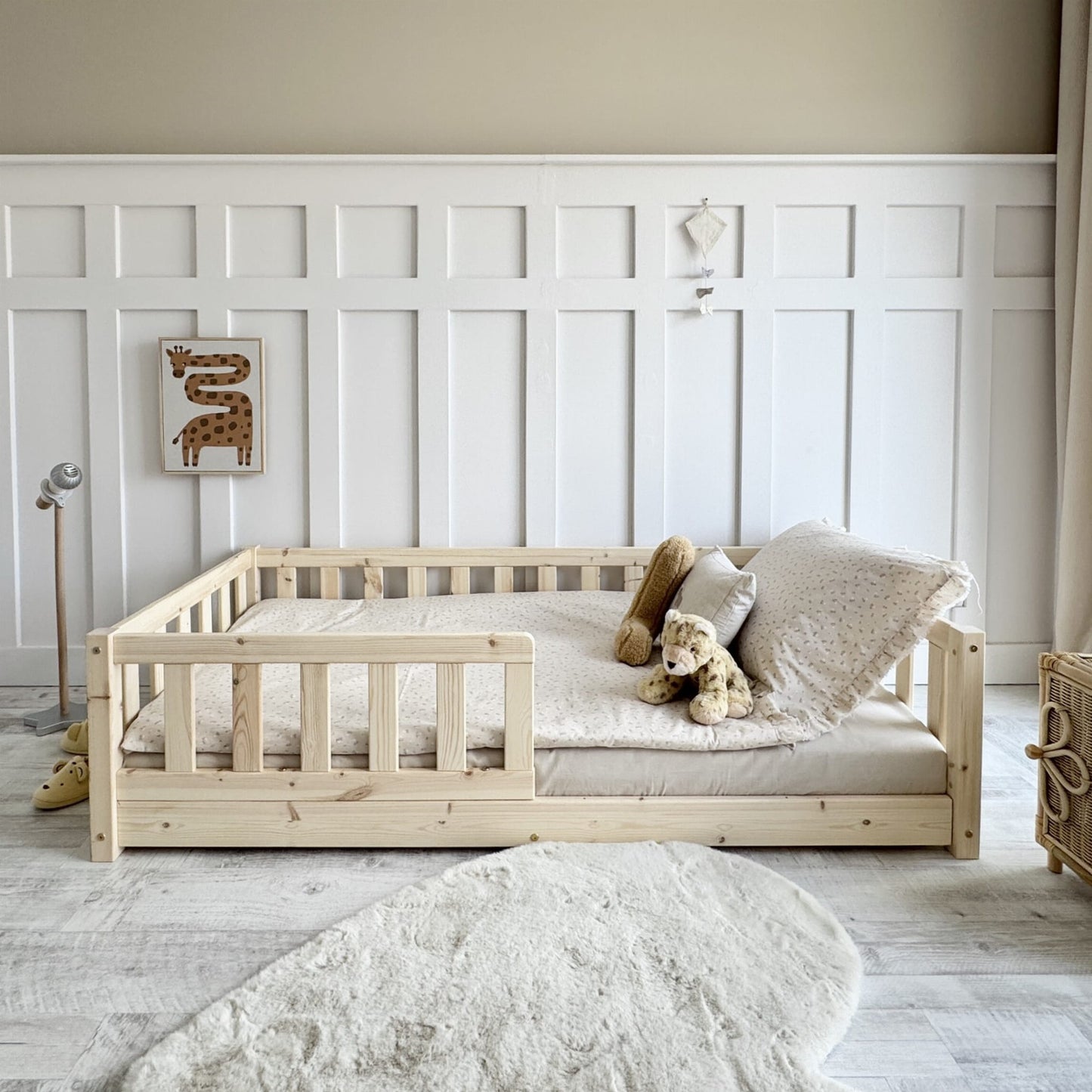 natural pine wood montessori floor bed with comfy pillows and soft toys in light bedroom 