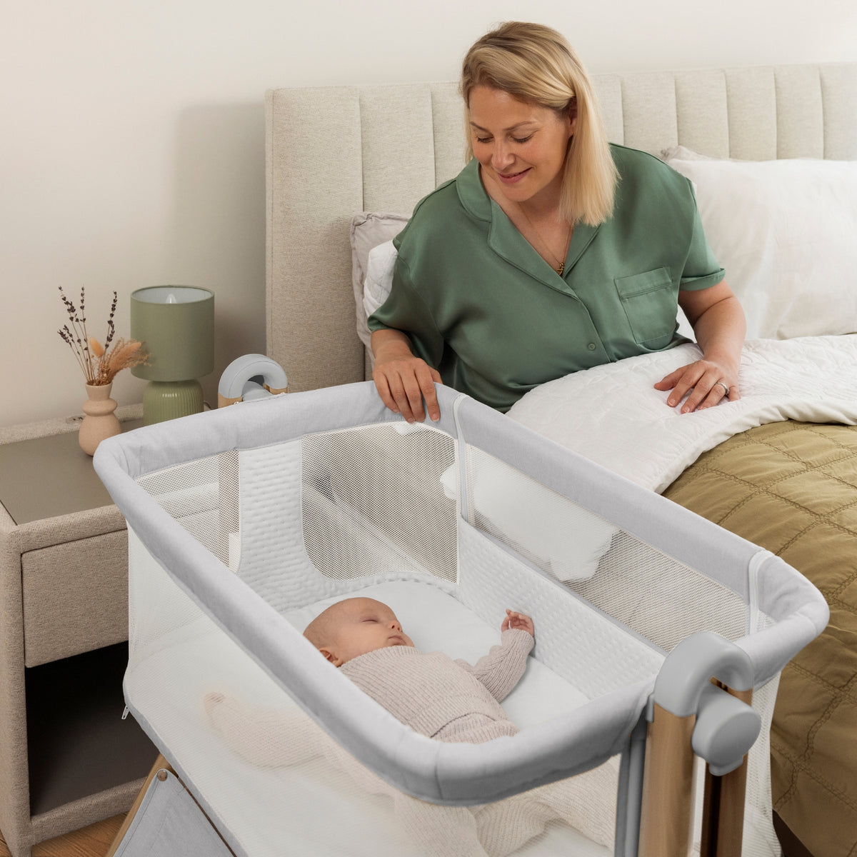 woman in bed looking at a baby in a grey Obaby Cloud bedside crib in modern bedroom 