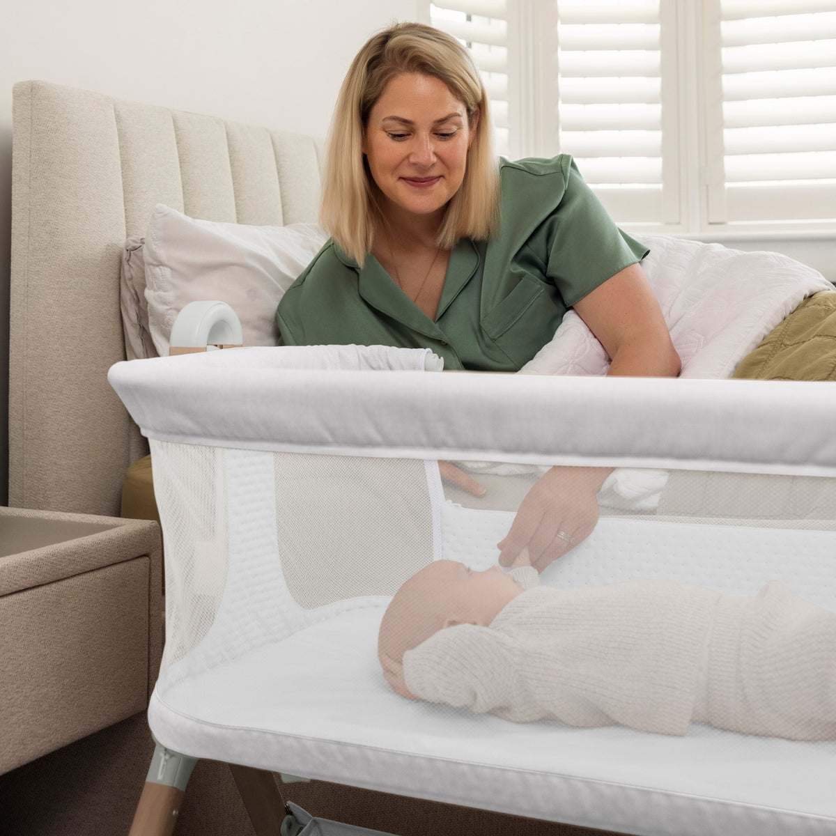 baby in a grey Obaby Cloud bedside crib next to a woman laying in a bed 