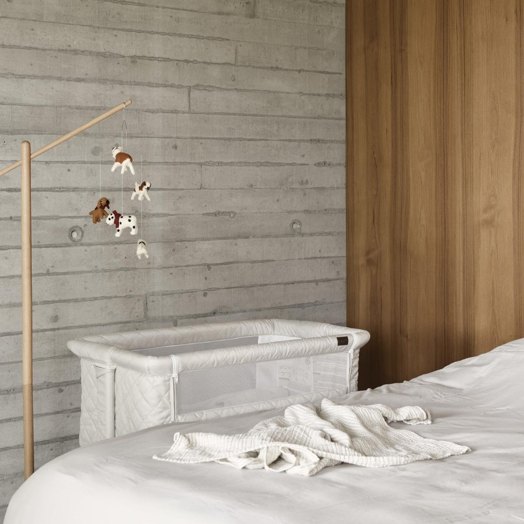quax baby cot mobile dogs hanging from wooden stand over next to me co-sleep beige crib in scandi bedroom