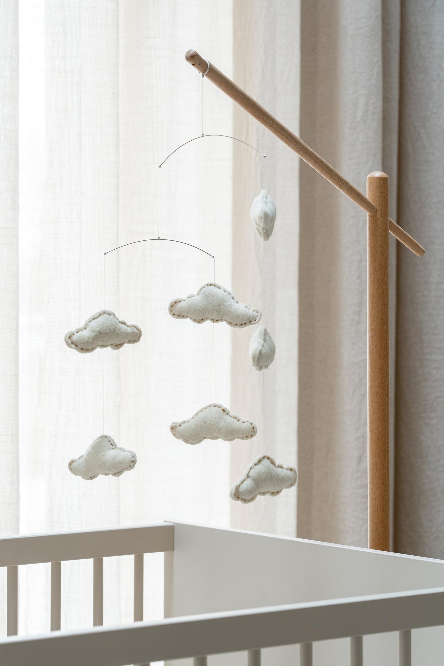 quax clouds baby cot mobile hanging from wooden stand over rocking wooden cot bed in calm nursery