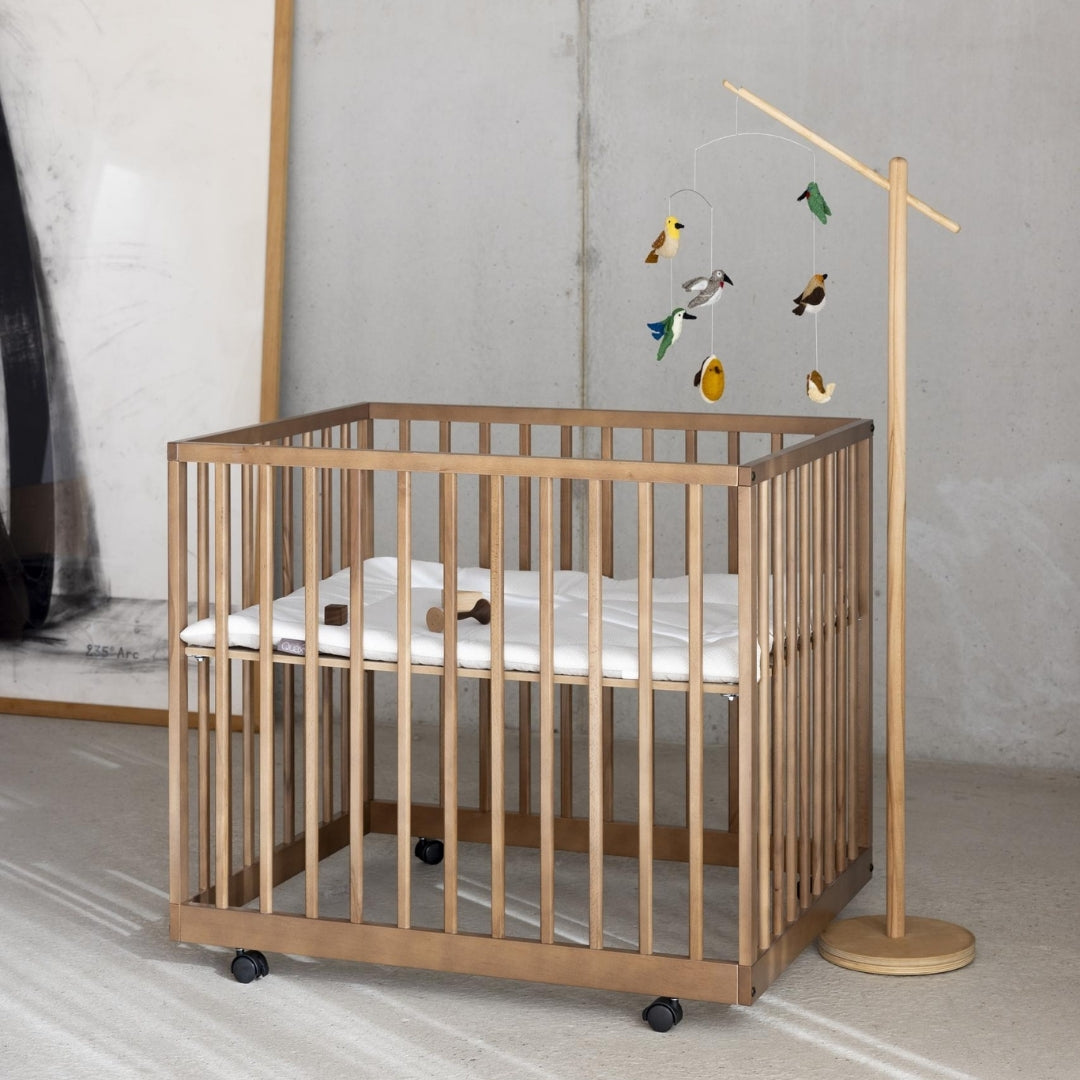 quax birds baby mobile hanging from wooden stand over wooden playpen in neutral scandi nursery
