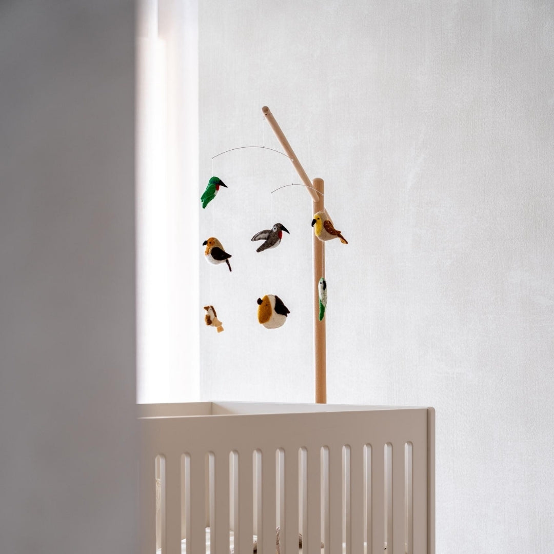 quax birds baby mobile hanging from wooden stand over simple white cot bed in neutral scandi nursery