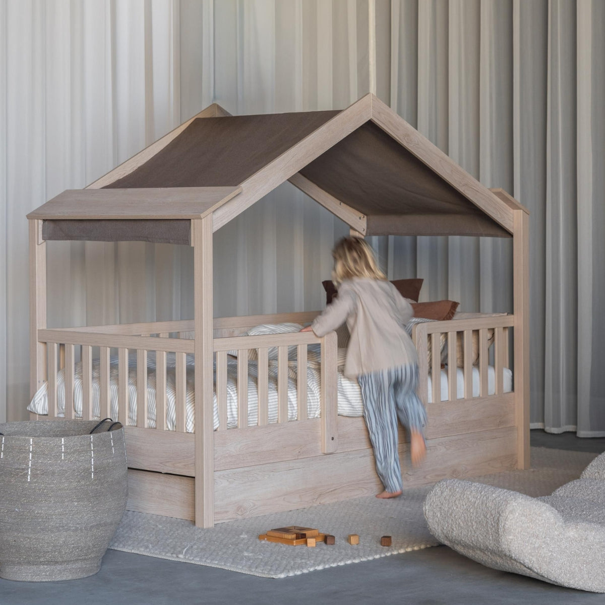 child climbing in to a quax chalet toddler montessori house bed in a modern bedroom with neutral decor